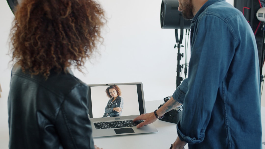 Photographer bearded guy is showing photos to mixed race model using laptop computer in studio talking pointing at screen. Business and devices concept.